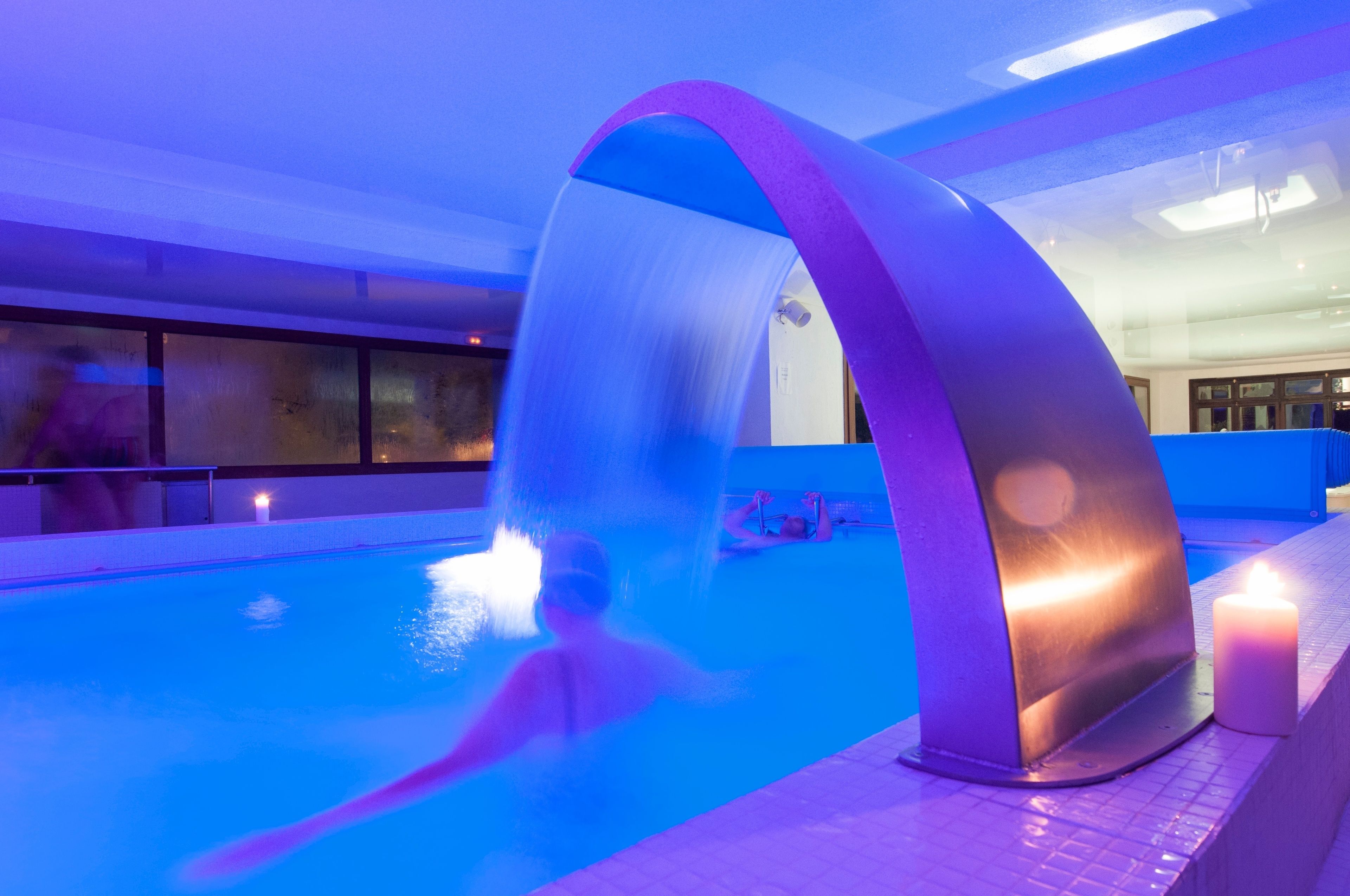 Una piscina interior con una fuente, una vela y una persona nadando.