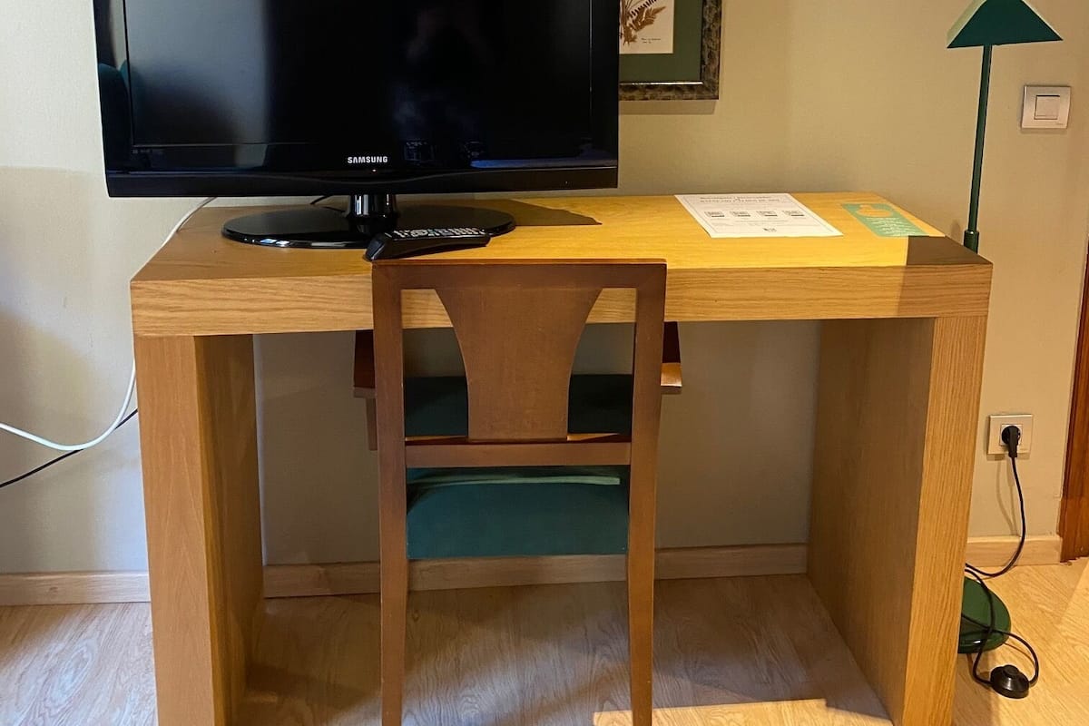 Uma mesa de madeira com uma TV de tela plana, uma cadeira, um abajur e um quadro na parede.