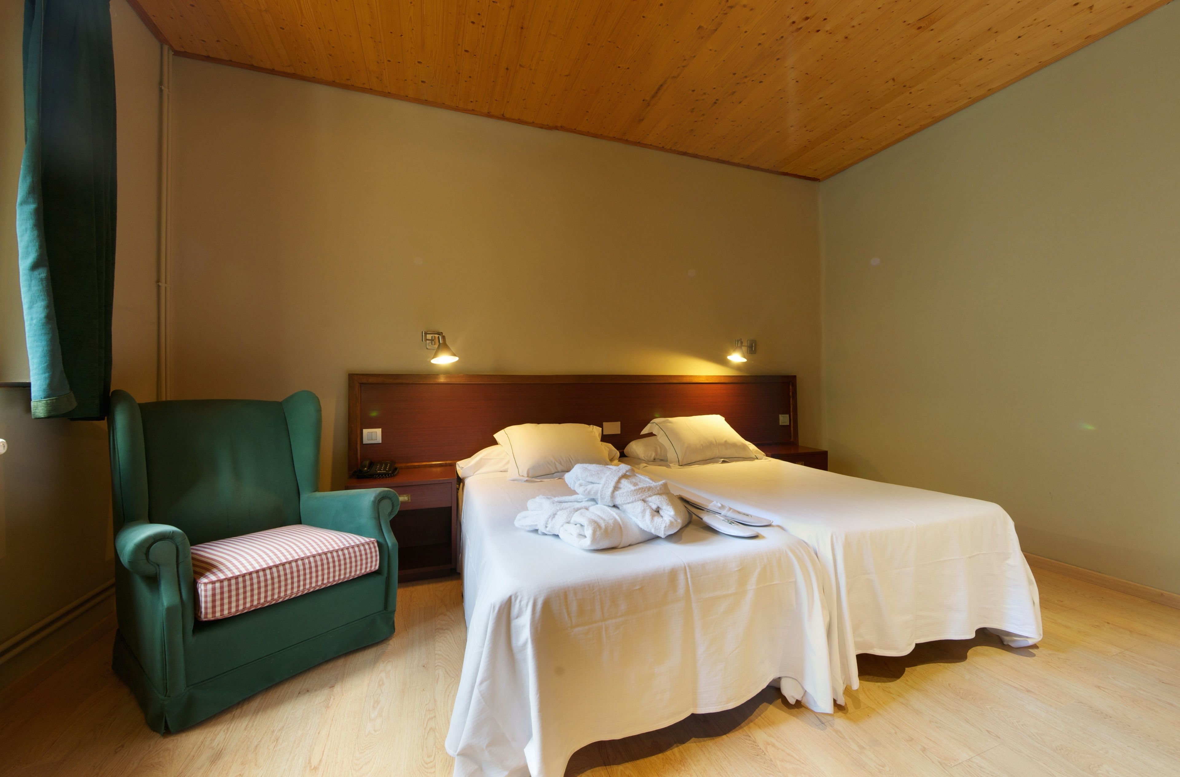 Una habitación con dos camas, un sillón verde y techo de madera.