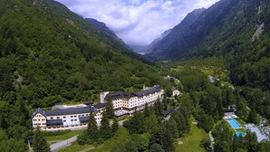 A large, multi-story hotel with a symmetrical facade, surrounded by lush green mountains and a valley. - Hotel Manantial- Balneari Caldes de Boi (La Vall de Boi)