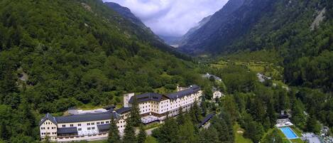 A large, multi-story hotel with a symmetrical facade, surrounded by lush green mountains and a valley.