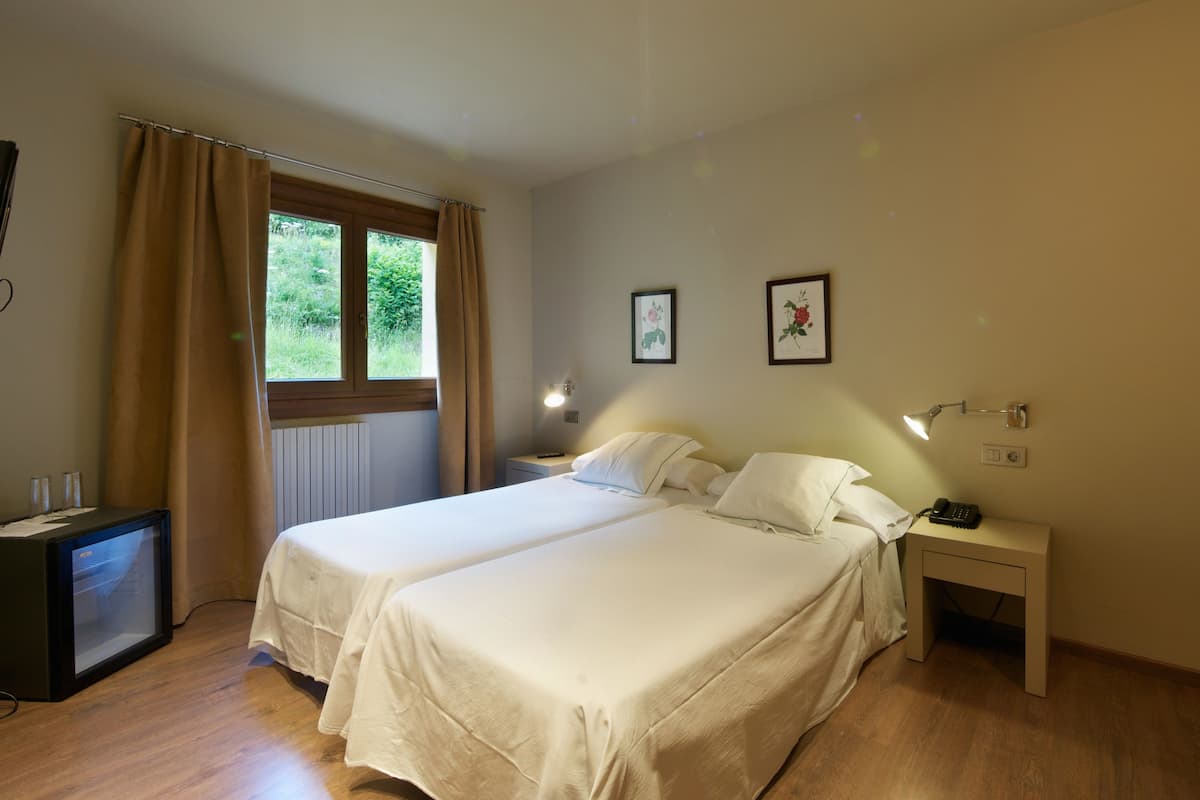 Quarto de hotel com duas camas, uma escrivaninha, uma televisão e uma janela com cortinas.