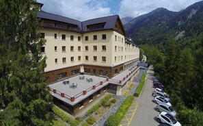 Un hotel de varios pisos con terraza en la azotea y aparcamiento, con montañas al fondo.