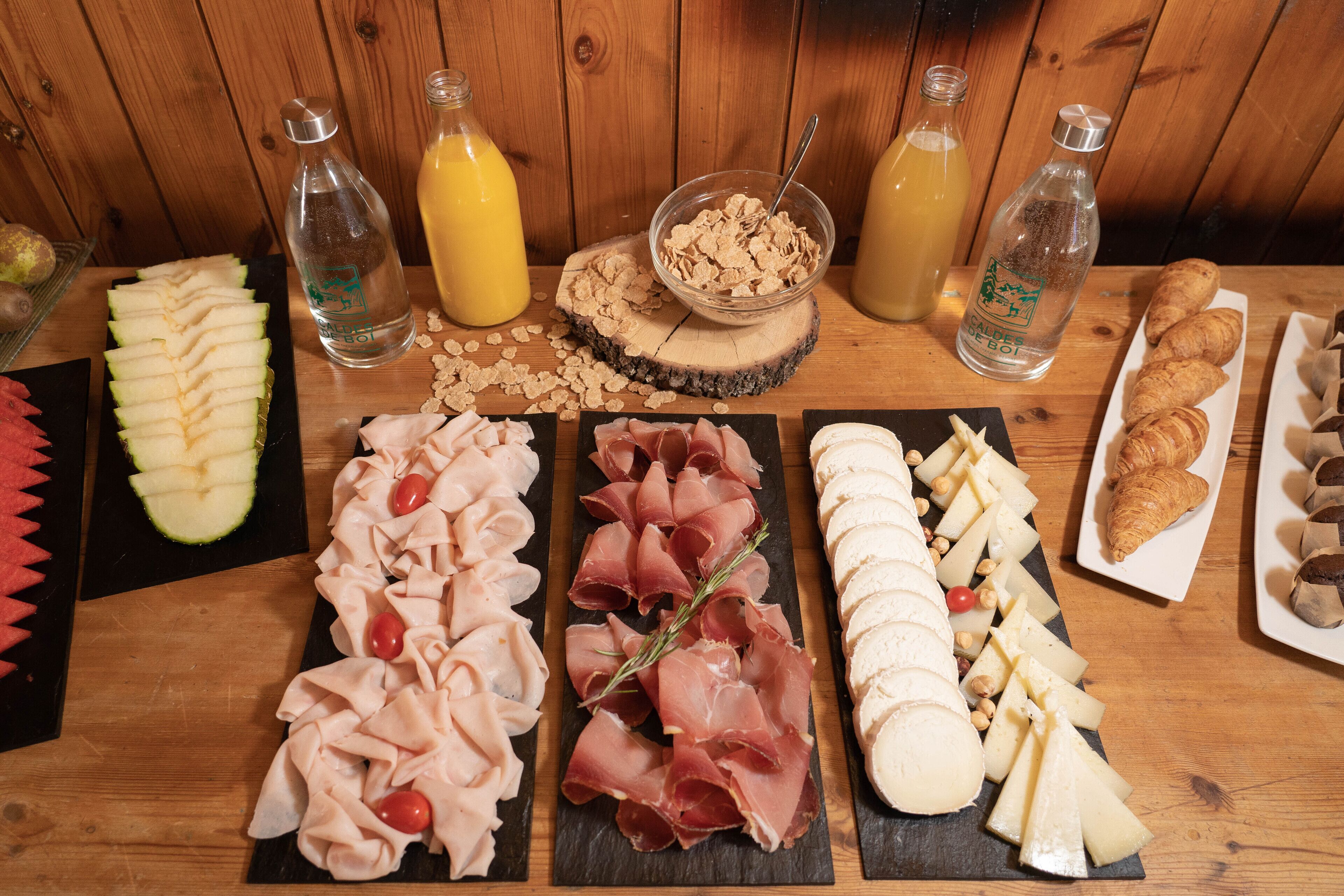 A wooden table with various food items including sliced apples, meats, cheeses, and pastries.