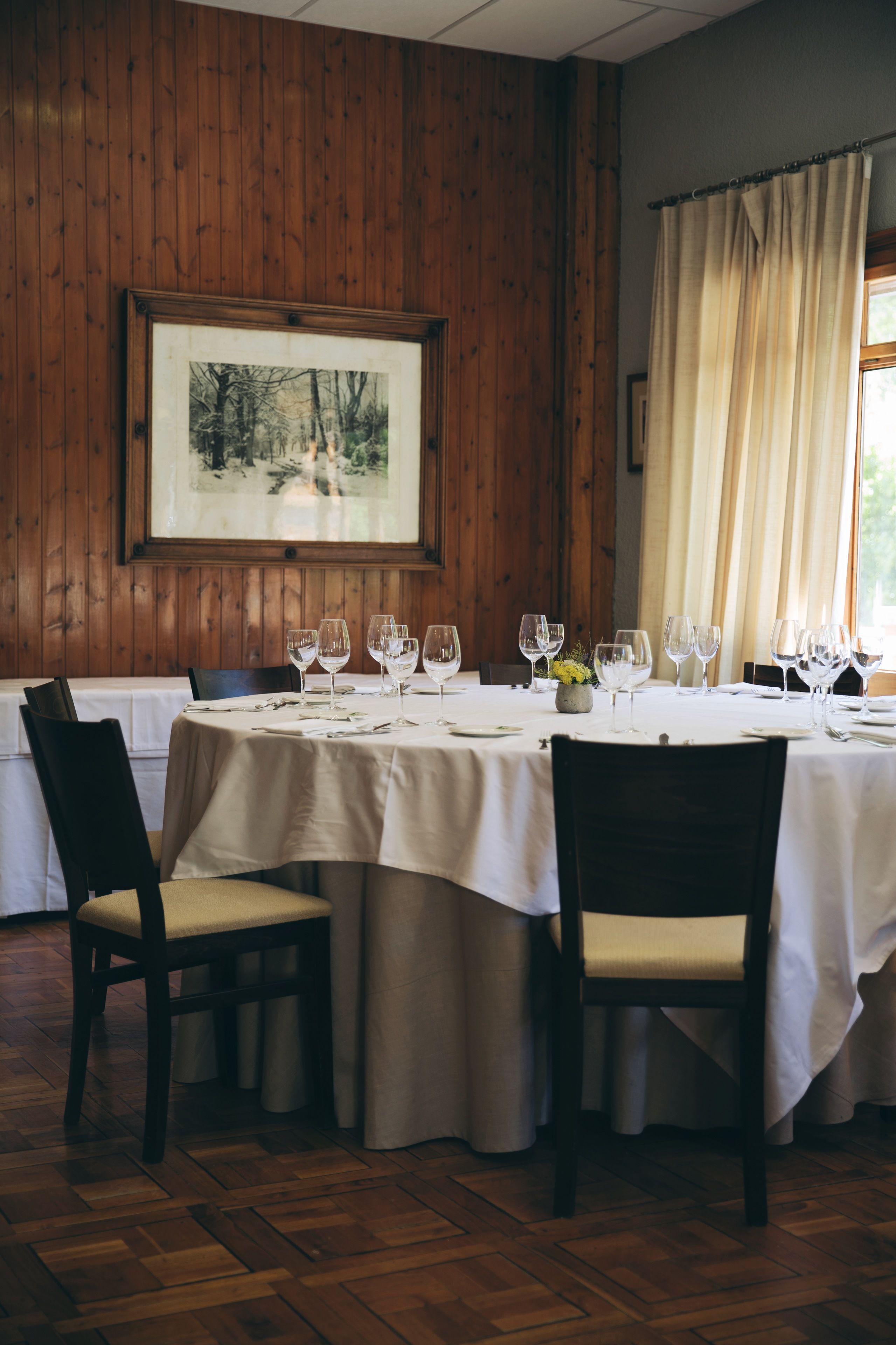 A dining area with a round table set for four, wooden paneled walls, and a framed picture on the wall.