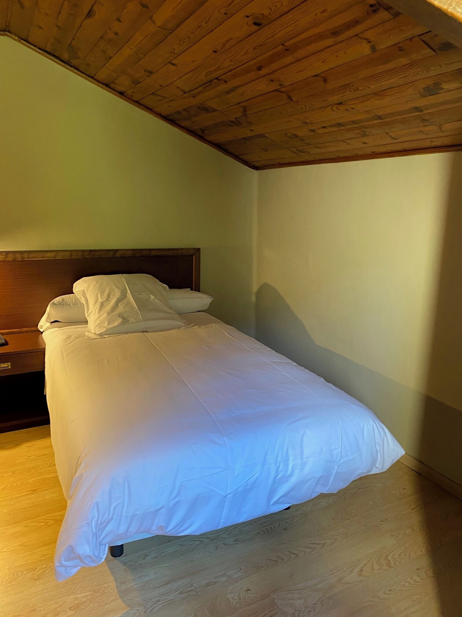 A single bed in a room with a wooden ceiling and a nightstand.