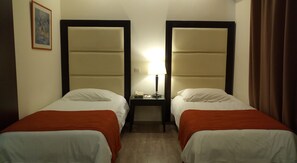 A hotel room with two single beds, a nightstand with a lamp, and a framed picture on the wall.