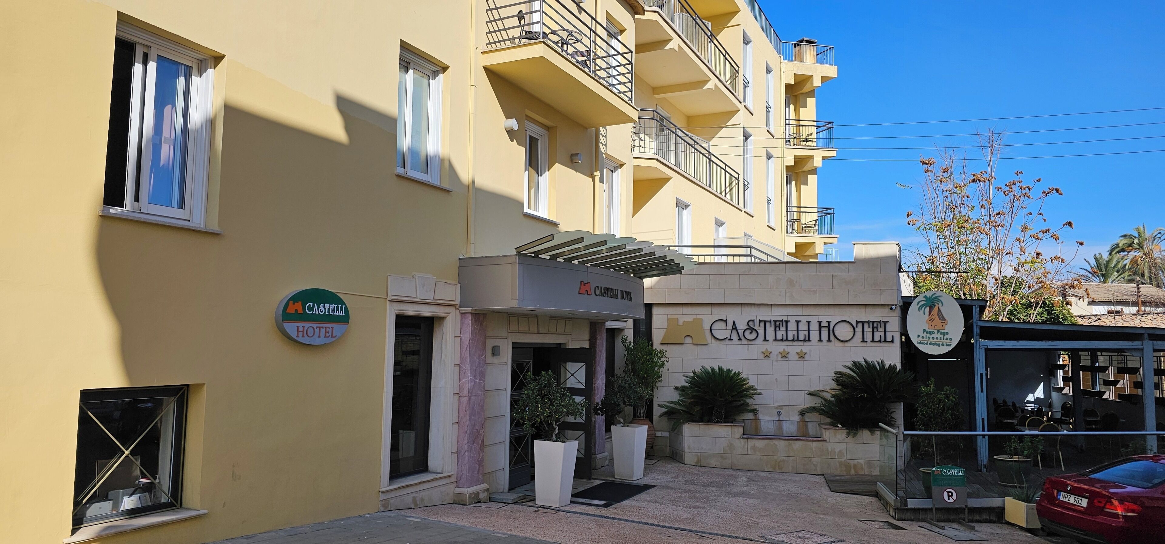 Ein Hotel Eingang mit einem Schild für das Castelli Hotel, einem Parkplatzschild und einem roten Auto davor.