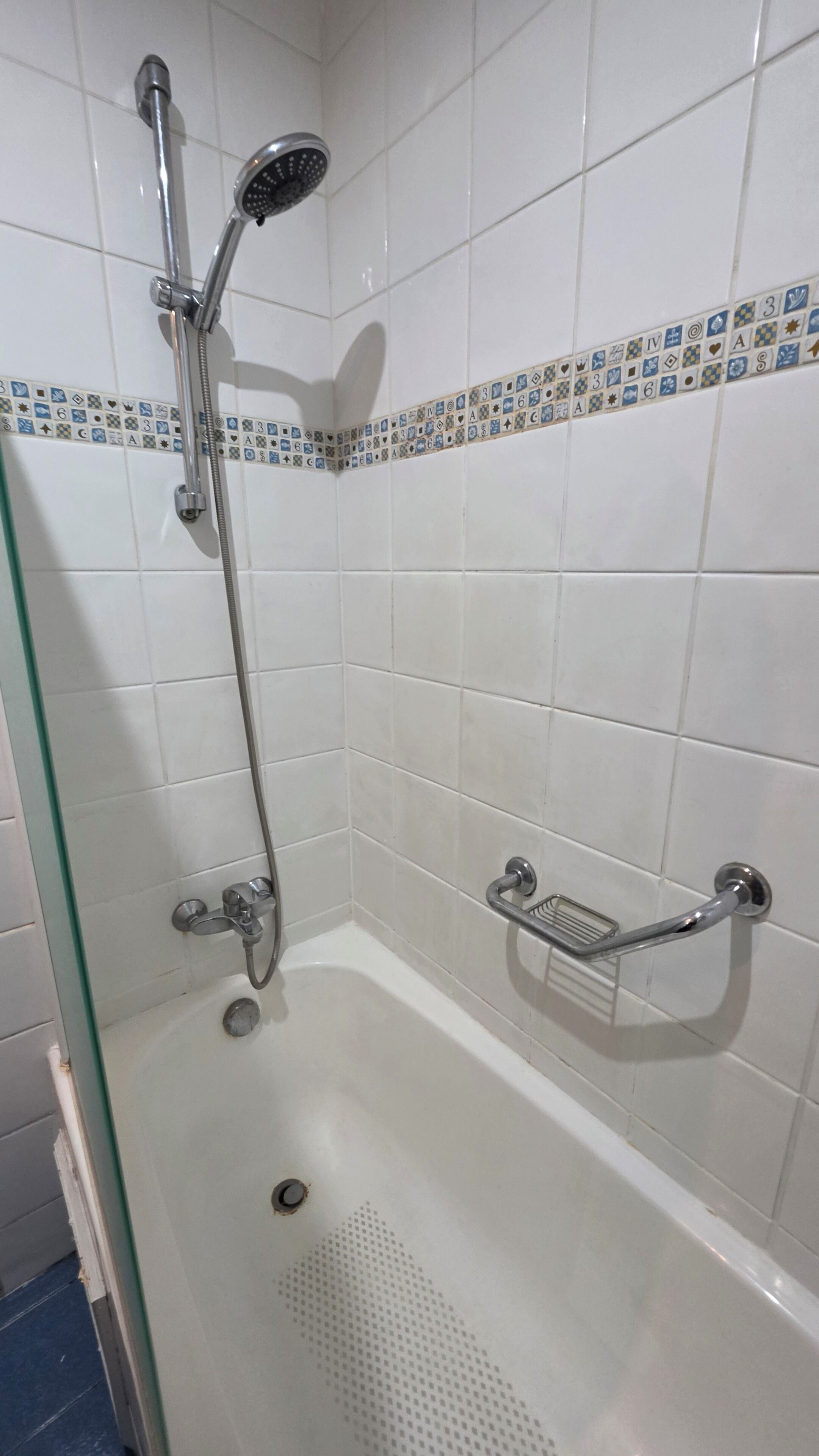 A shower area with a glass door, a handheld showerhead, a handheld shower attachment, and a handheld shower head mounted on the wall.