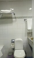 Un baño con inodoro, dispensador de toallas de papel, un cubo de basura y un perchero para toallas.