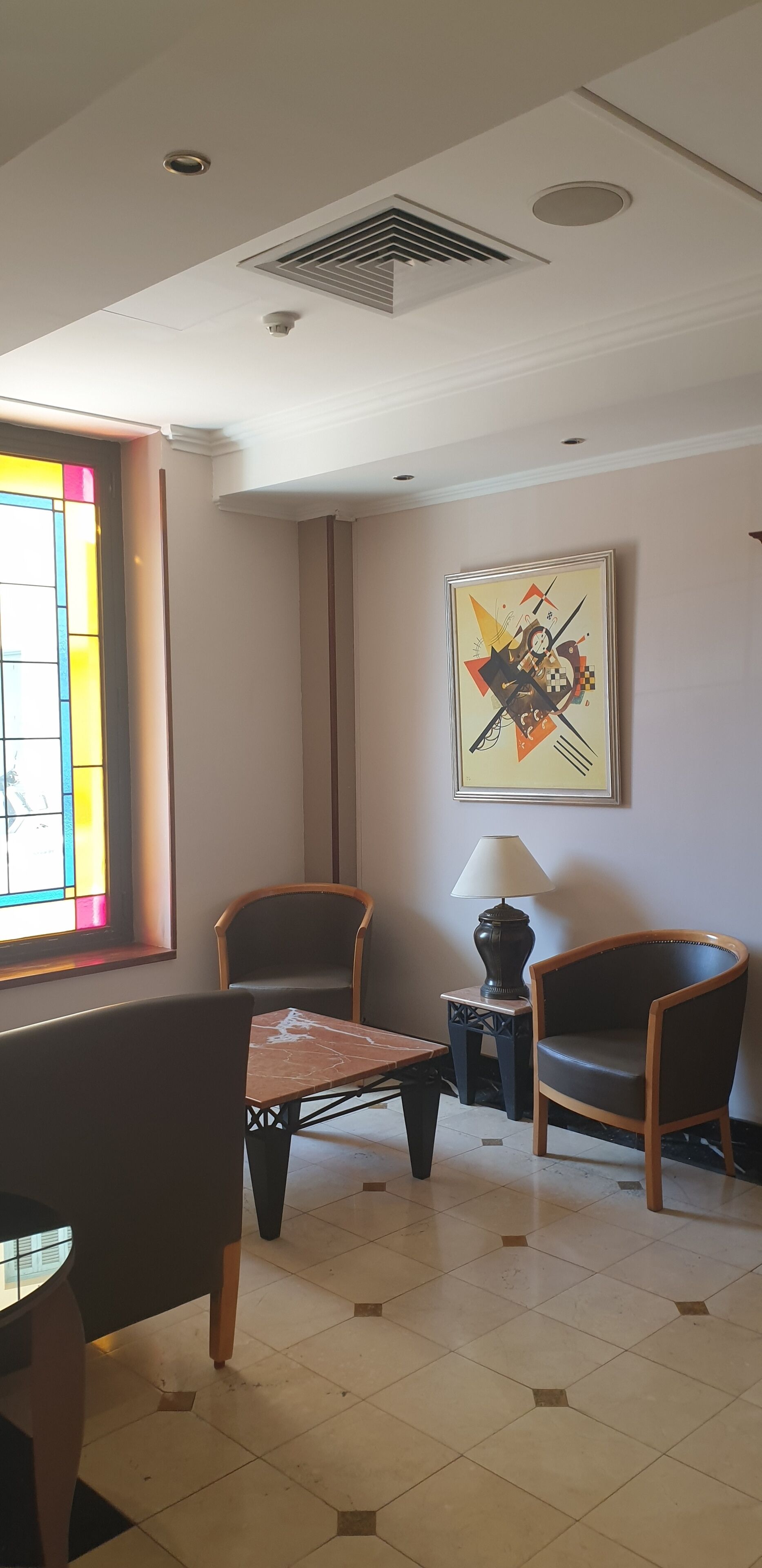 Habitación de hotel con una mesa de comedor, dos sillas, una lámpara y una obra de arte colgada en la pared.