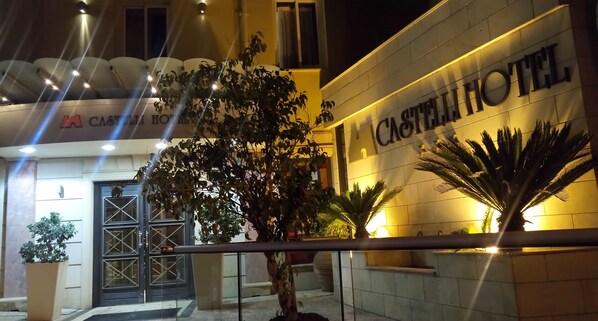 Exterior del hotel Castellini, con una entrada destacada, una planta grande en maceta y una fachada bien iluminada.