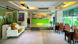 A hotel lobby with a reception desk, seating area, and a view of greenery outside. - Centric Place Hotel (Bangkok)