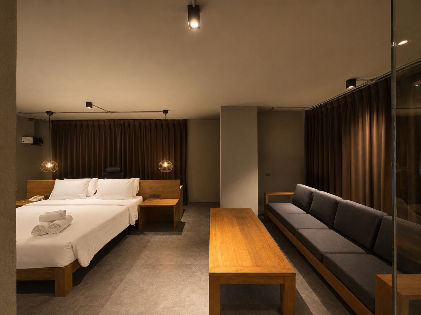 Ein modernes Hotelzimmer mit einem Bett, einer Couch, einem Holztisch und einem Schreibtisch mit einer Lampe.