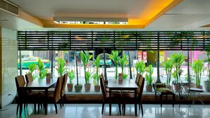 A restaurant with a modern interior, featuring a long table with chairs, potted plants, and a view of the street outside. - Centric Place Hotel (Bangkok)