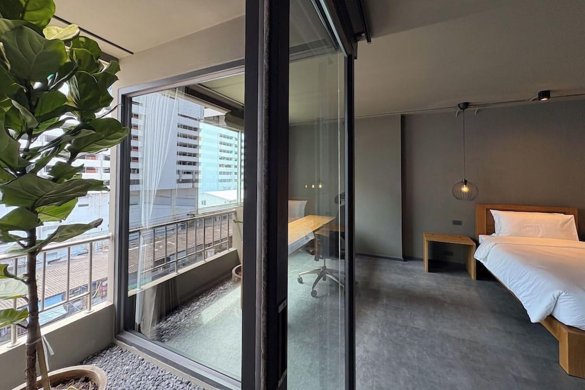 A modern hotel room with a large sliding glass door, a bed, a desk, and a potted plant.