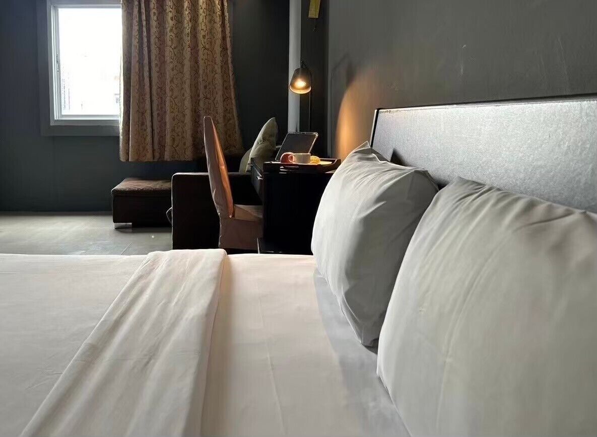 Habitación de hotel impecable con una cama grande, un escritorio con una computadora portátil y una ventana con cortinas.
