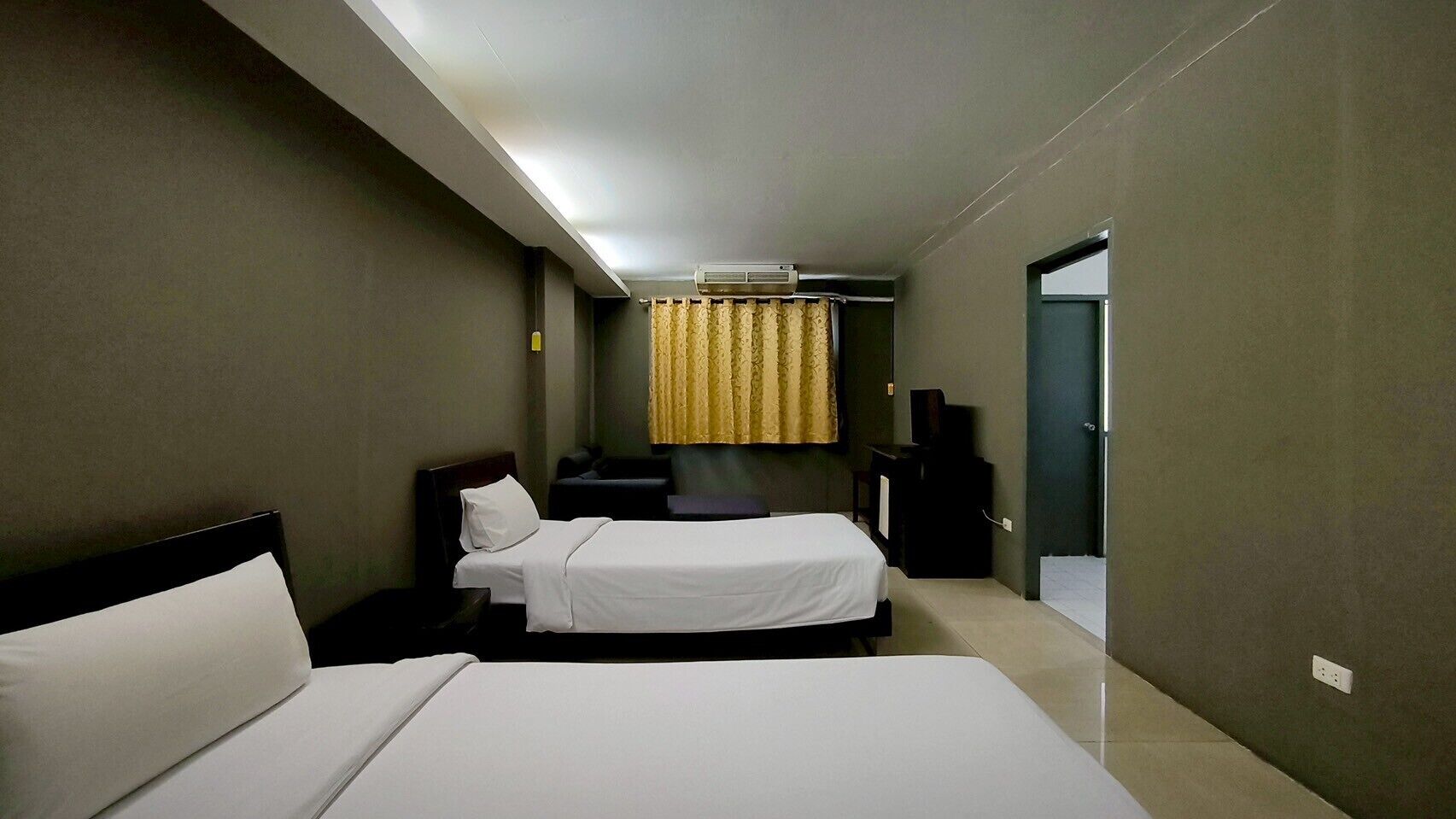 Una habitación de hotel con dos camas, un escritorio, una silla, un televisor y una ventana con cortinas.