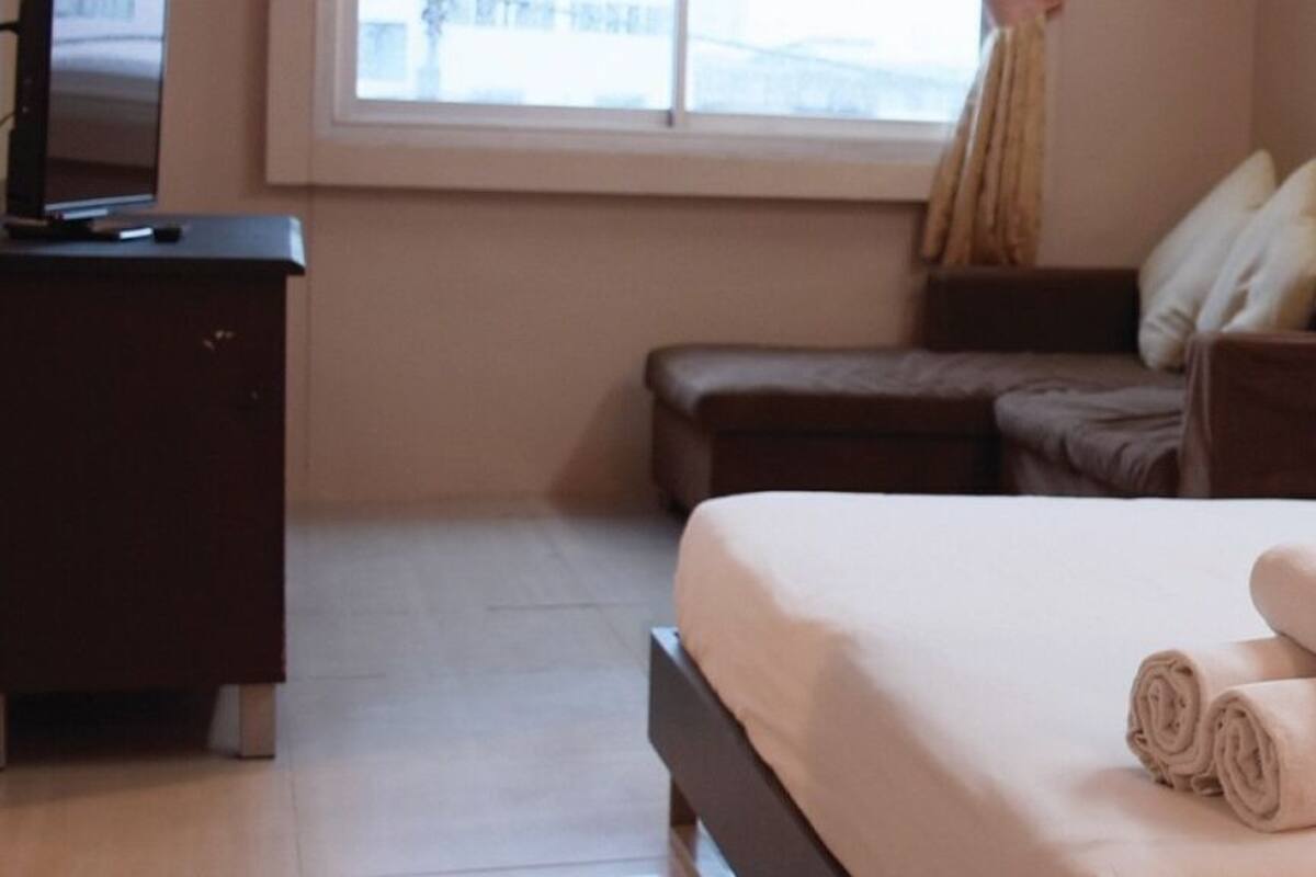 A hotel room with a bed, a nightstand, a dresser, and a window.
