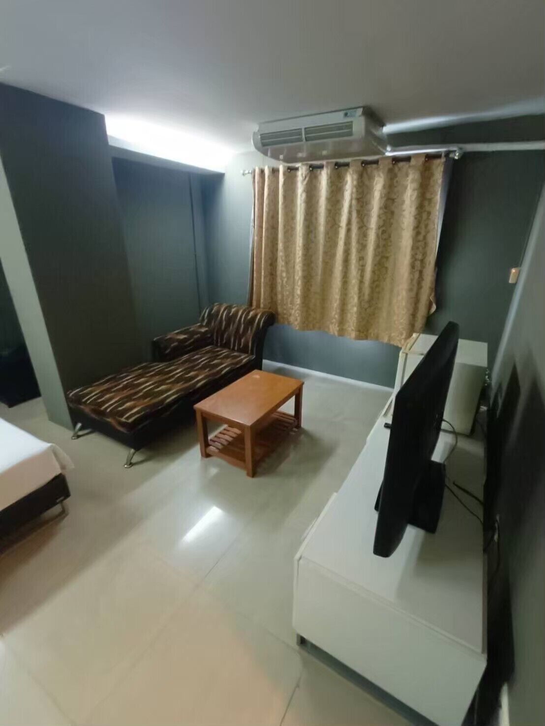 A compact room with a sofa, a small table, a TV, and an air conditioning unit.
