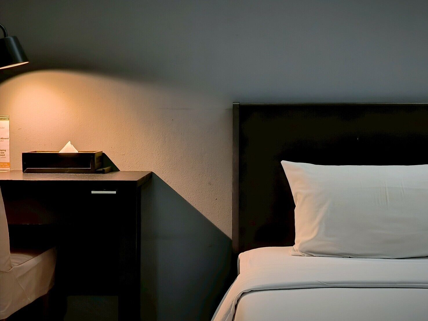A neatly made bed with white bedding, a black headboard, and a bedside table with a lamp and a tissue box.