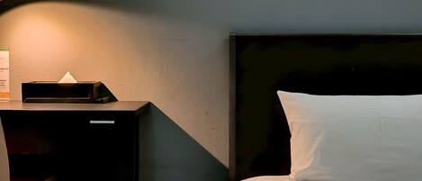A neatly made bed with white bedding, a black headboard, and a bedside table with a lamp and a tissue box.