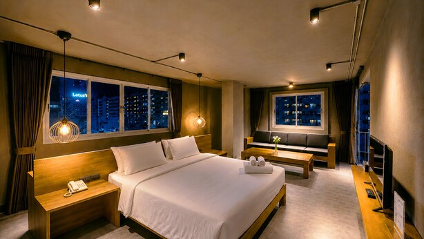 A hotel room with a large bed, bedside tables, a sofa, a TV, and windows with city views. - Centric Place Hotel (Bangkok)