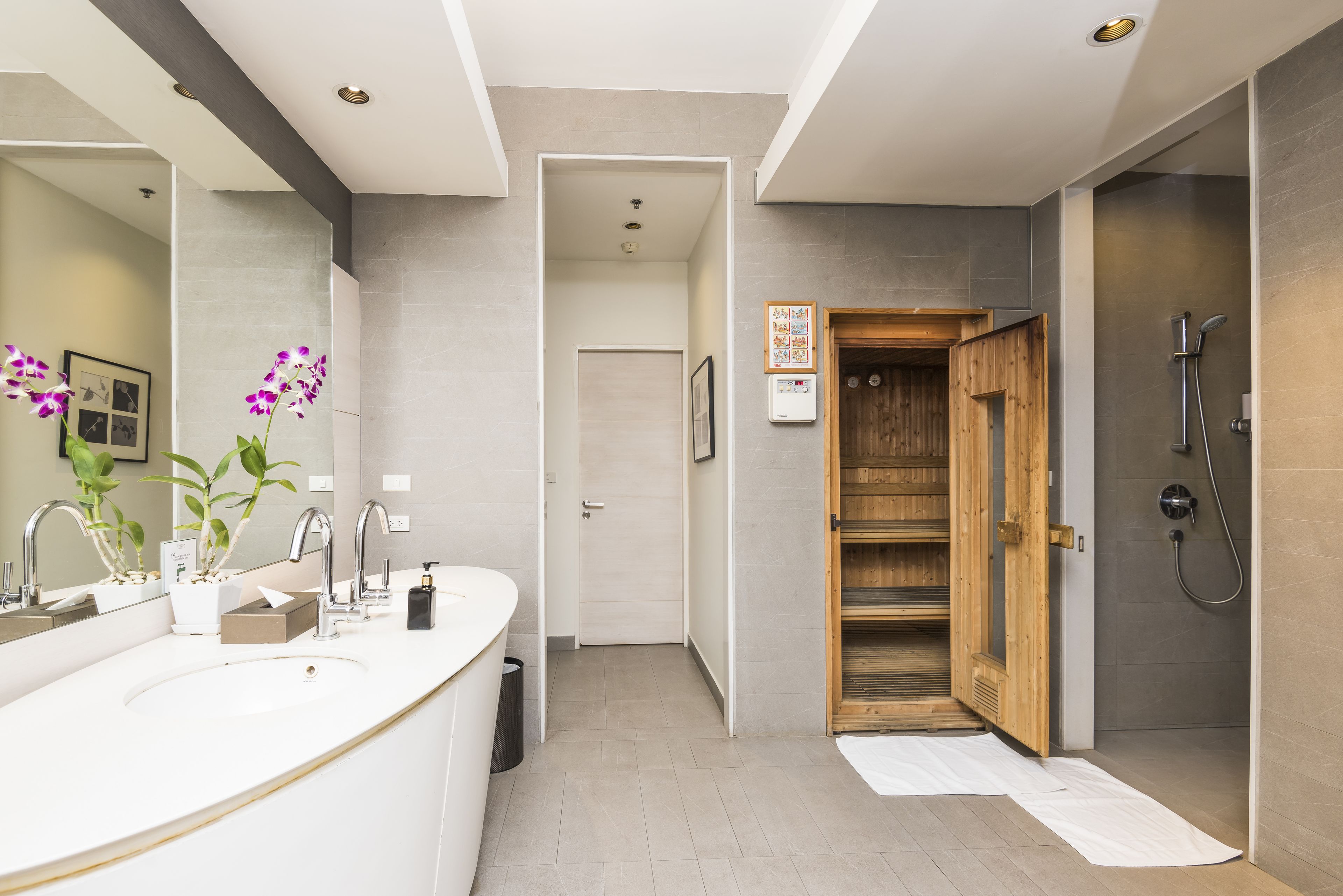 A modern bathroom with a large white sink, a wooden shower enclosure, and a visible door leading to another room.