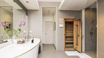 A modern bathroom with a large white sink, a wooden shower enclosure, and a visible door leading to another room.