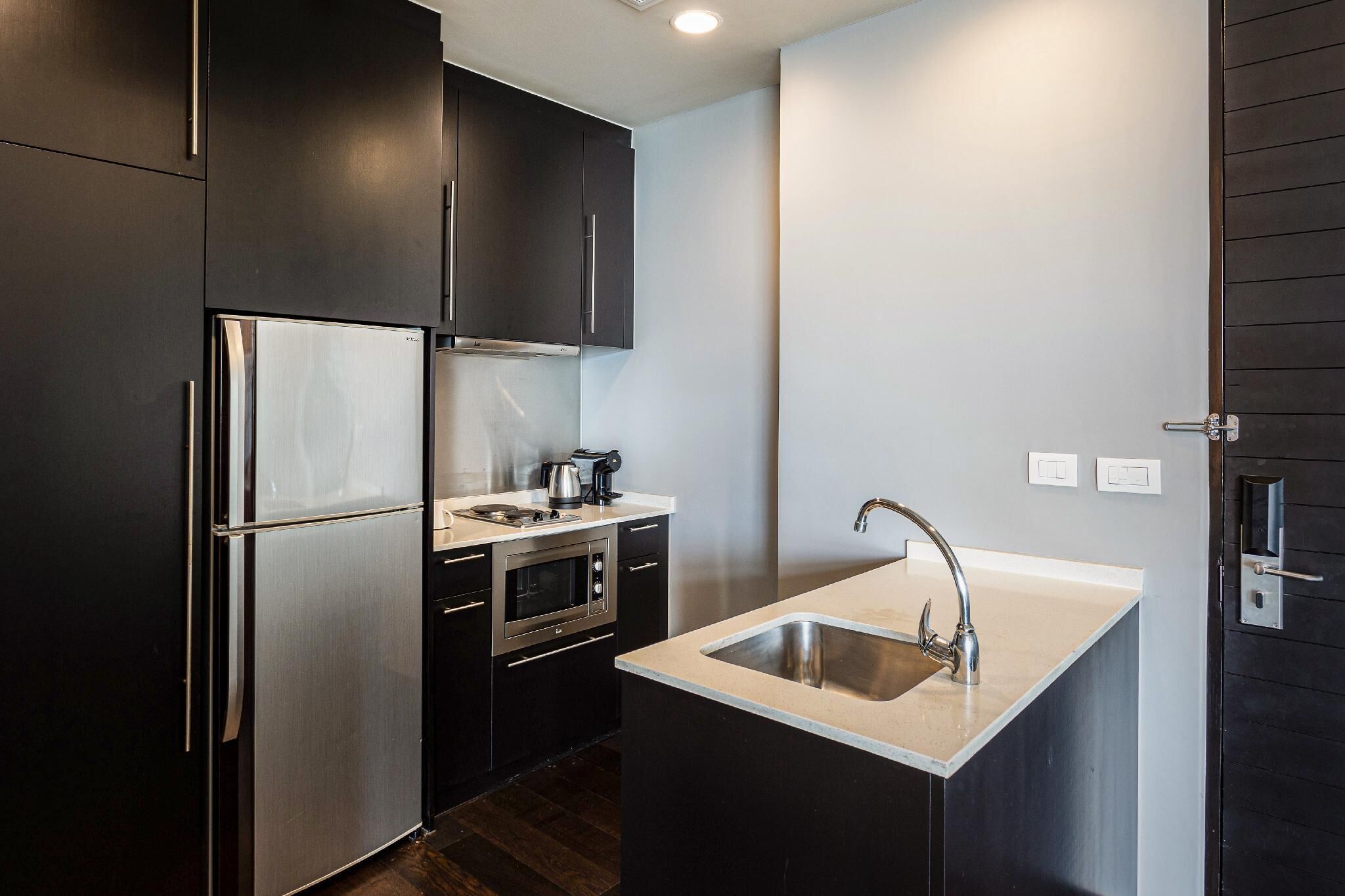 A compact kitchen with dark cabinetry, a stainless steel refrigerator, an oven, and a sink.