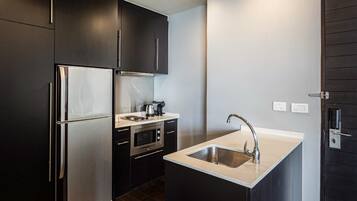 A compact kitchen with dark cabinetry, a stainless steel refrigerator, an oven, and a sink.