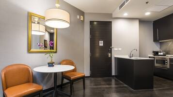Una cocina moderna con suelo de madera oscura, una mesa redonda con dos sillas, una lámpara colgante y una puerta negra con un cartel pequeño.