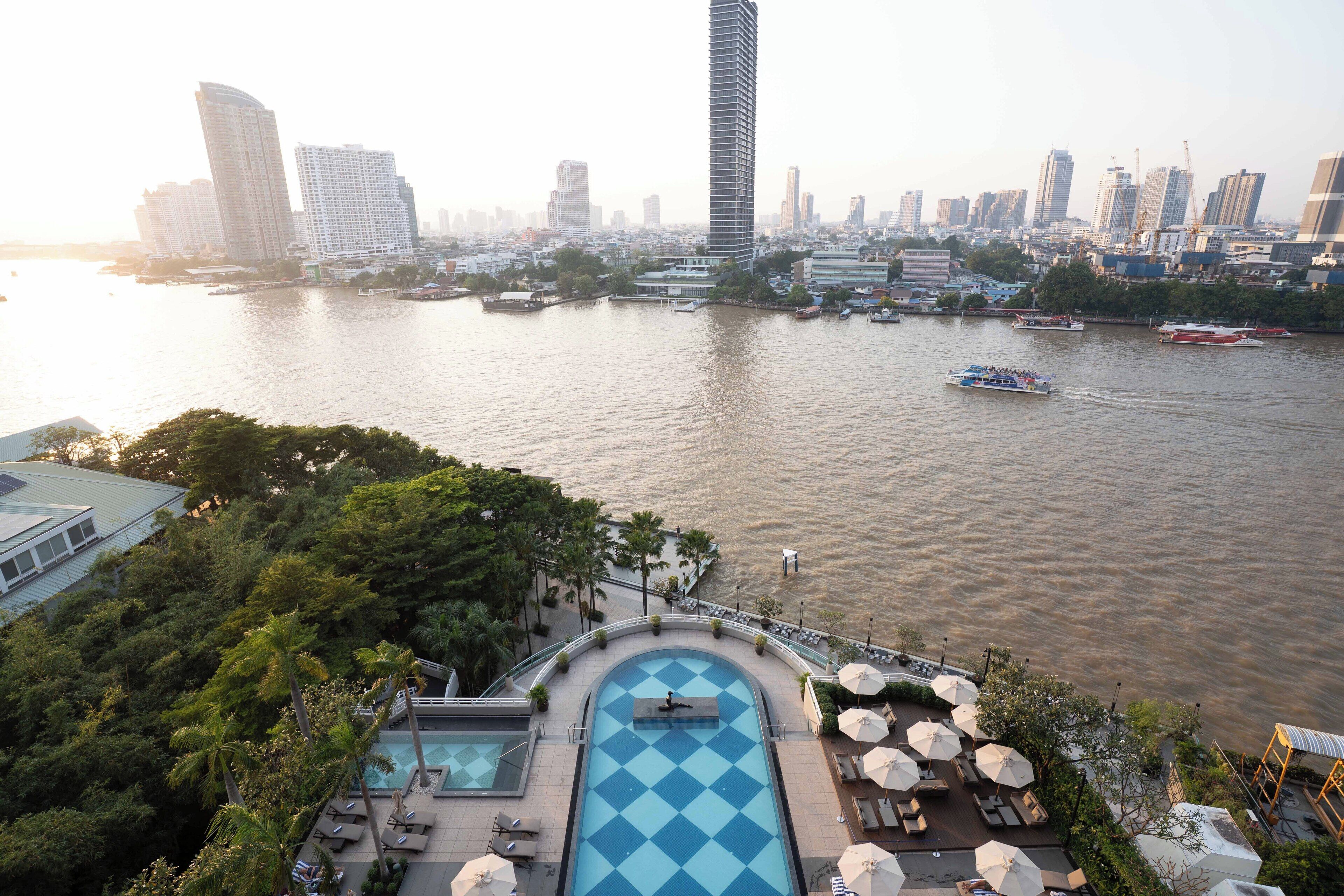 Un hotel moderno de gran altura con piscina y tumbonas, con vista a un río y barcos.