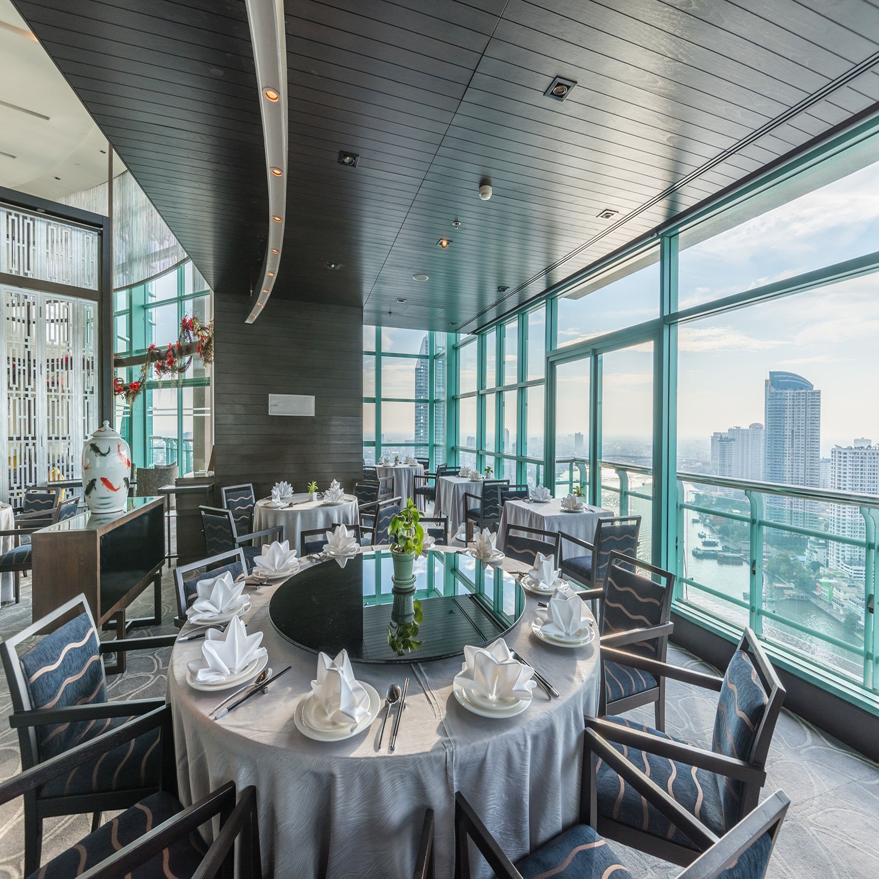 Un comedor moderno con mesas redondas, sillas y vistas a la ciudad a través de amplios ventanales.
