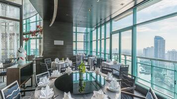 Un comedor moderno con mesas redondas, sillas y vistas a la ciudad a través de amplios ventanales.