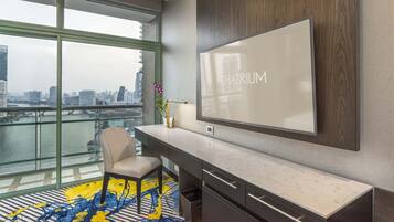 A modern hotel room with a large TV, a city view, a desk, and a chair.
