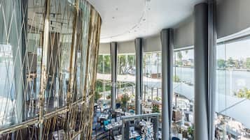 Un restaurante moderno con pared de vidrio curva, alfombra azul y mesas dispuestas para comer.
