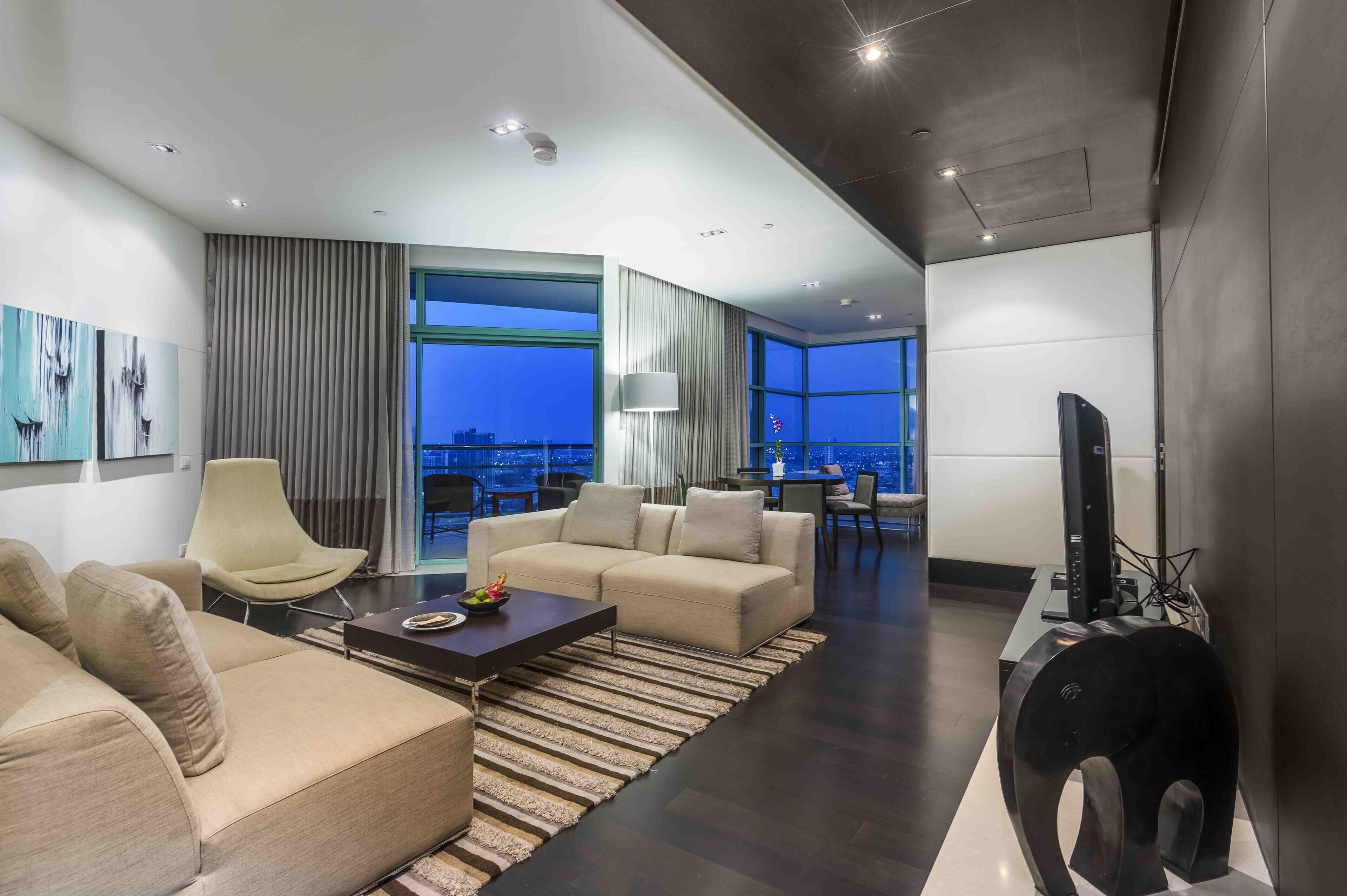 A modern living room with a sofa, armchair, and coffee table, a TV, and a view of the city at night.