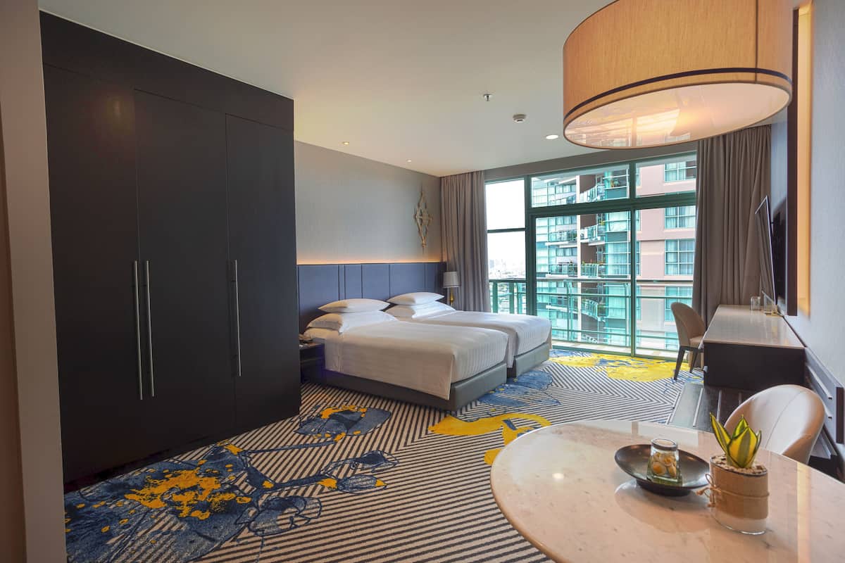 Une chambre d’hôtel dotée d’un grand lit, d’un bureau, d’une chaise, d’une table à manger et offrant une vue sur la ville grâce à de grandes fenêtres.