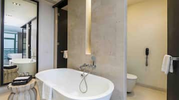 Un baño moderno con una bañera independiente, un inodoro y un espejo grande.