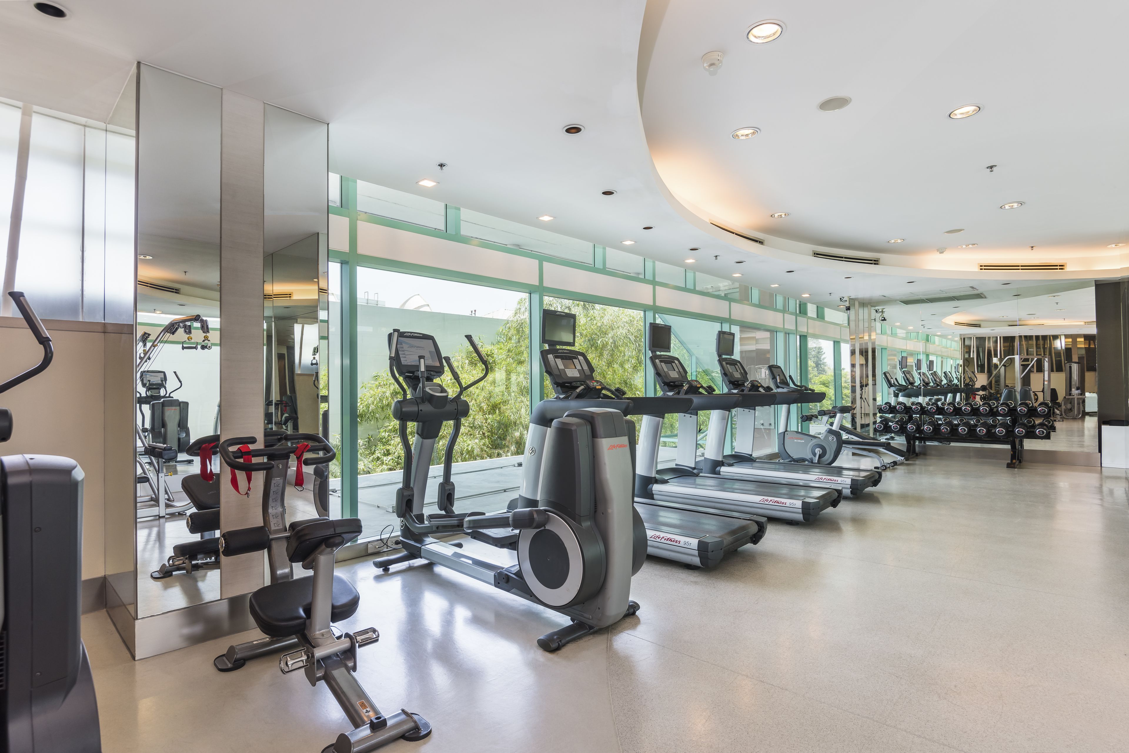 Un gimnasio moderno con máquinas de cardio, estaciones de pesas y un espejo grande que refleja el espacio.