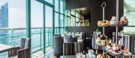 A modern dining area with a tiered dessert display, seating arrangements, and a view of the cityscape.