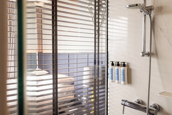 A bathroom with a shower, a toilet, and a sink. There are three bottles of toiletries on the wall. - Chatrium Hotel Riverside Bangkok (Bangkok)