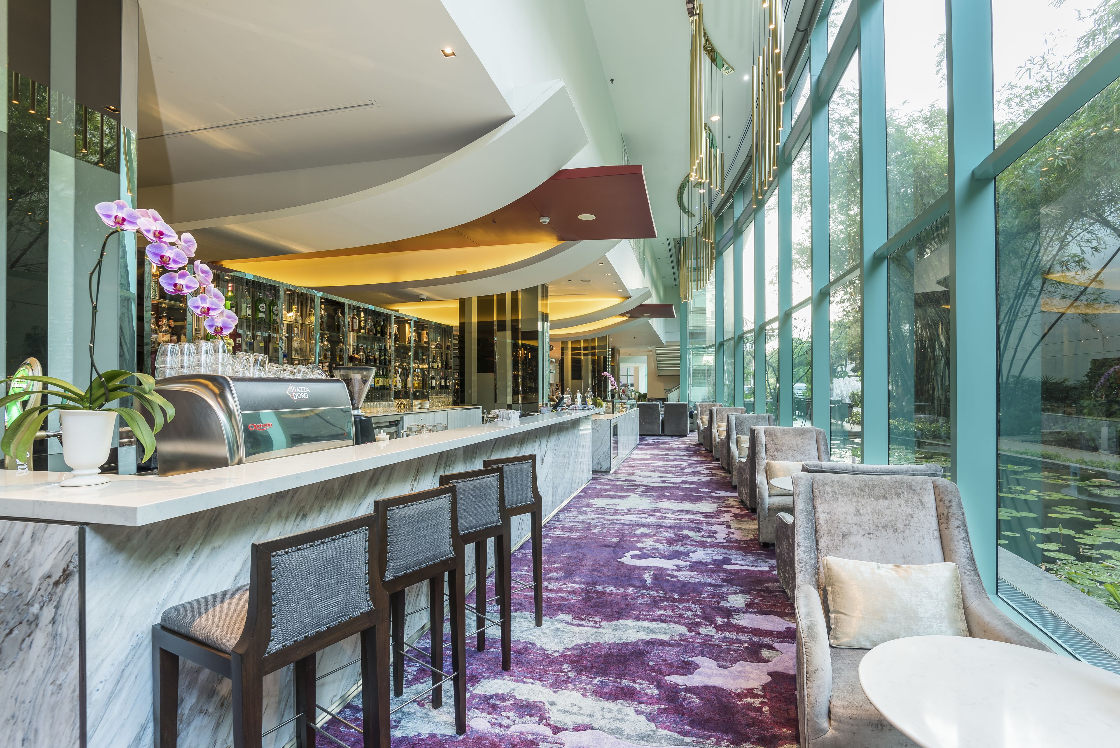 Uma área de bar moderna com bancada de mármore, banquetas e uma grande janela com vista para o exterior.