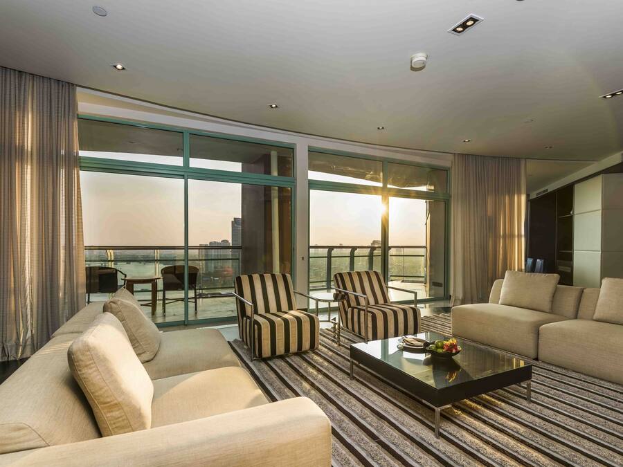 Una habitación de hotel moderna con un balcón grande, un conjunto de sofá, sillones a rayas y una mesa de centro.