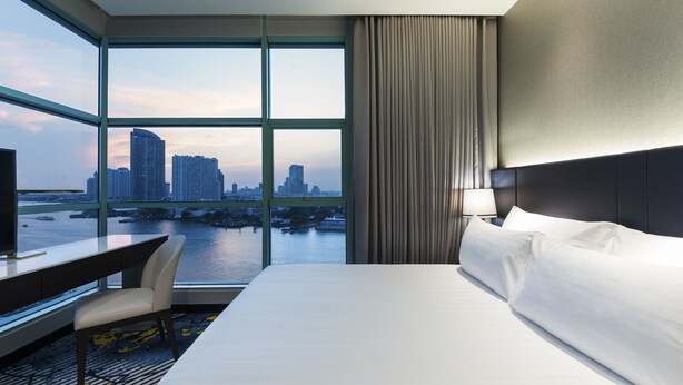 Una habitación de hotel con un ventanal grande, una cama, un escritorio y una silla.