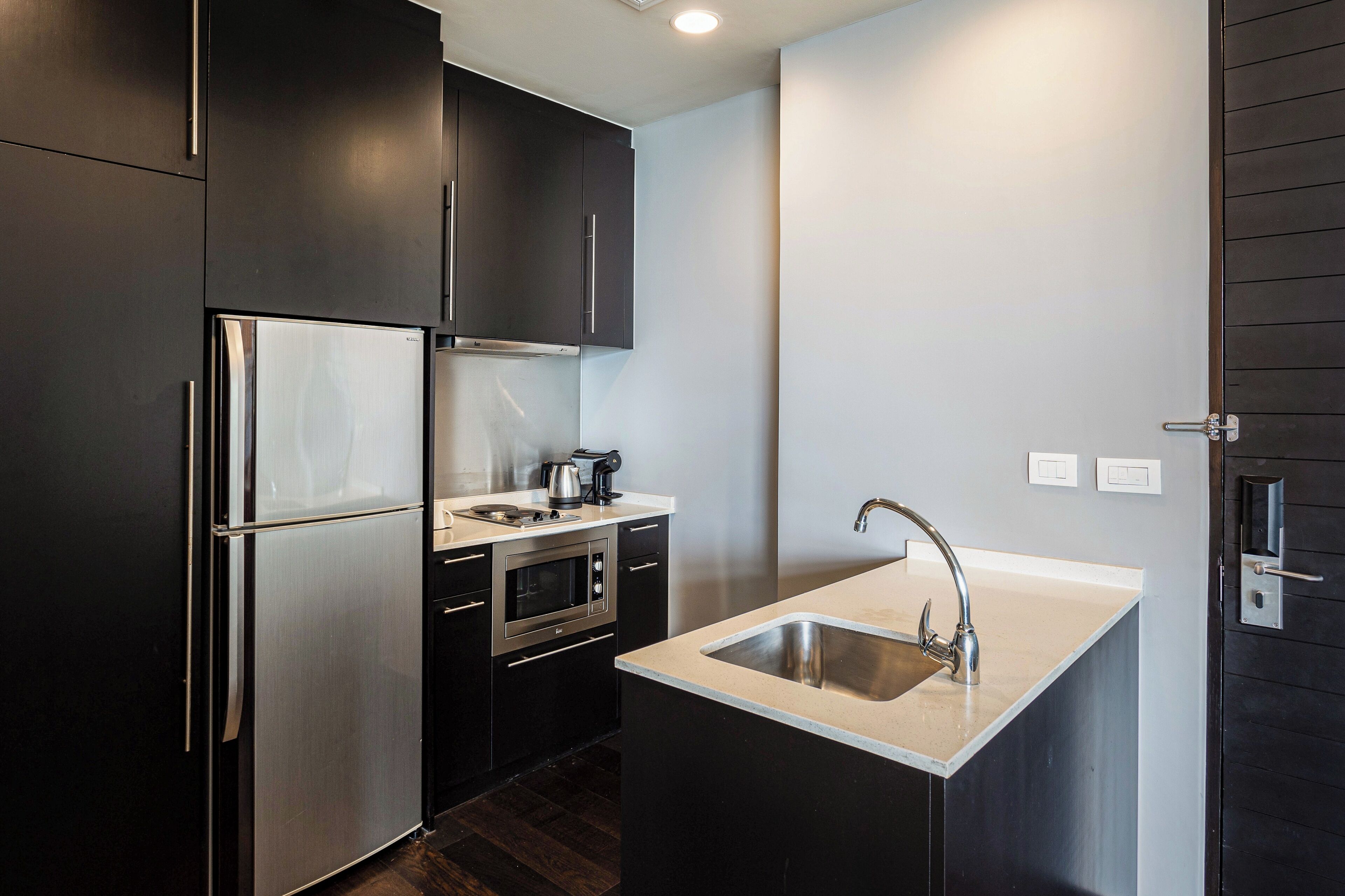 Una cocina compacta con muebles oscuros, un refrigerador de acero inoxidable, un horno, un lavamanos y una encimera.