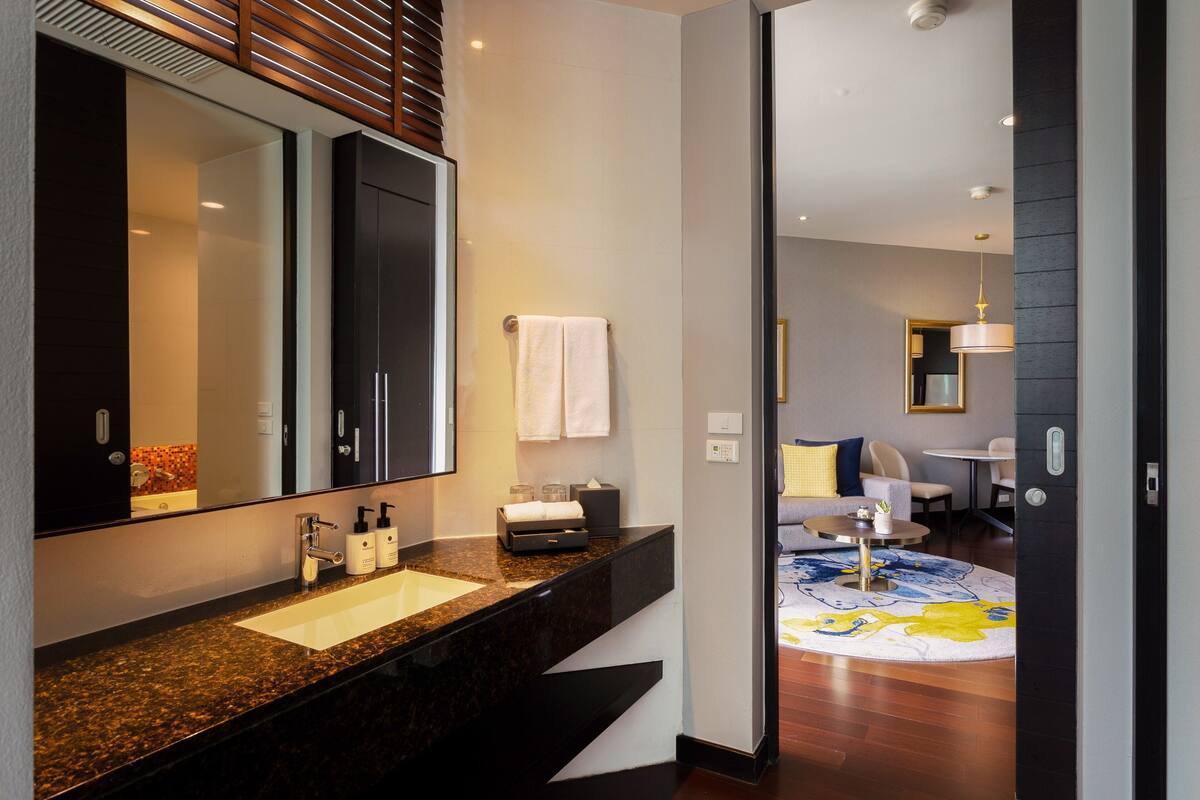 Une salle de bain moderne avec un grand miroir, un plan de toilette foncé et un lavabo.