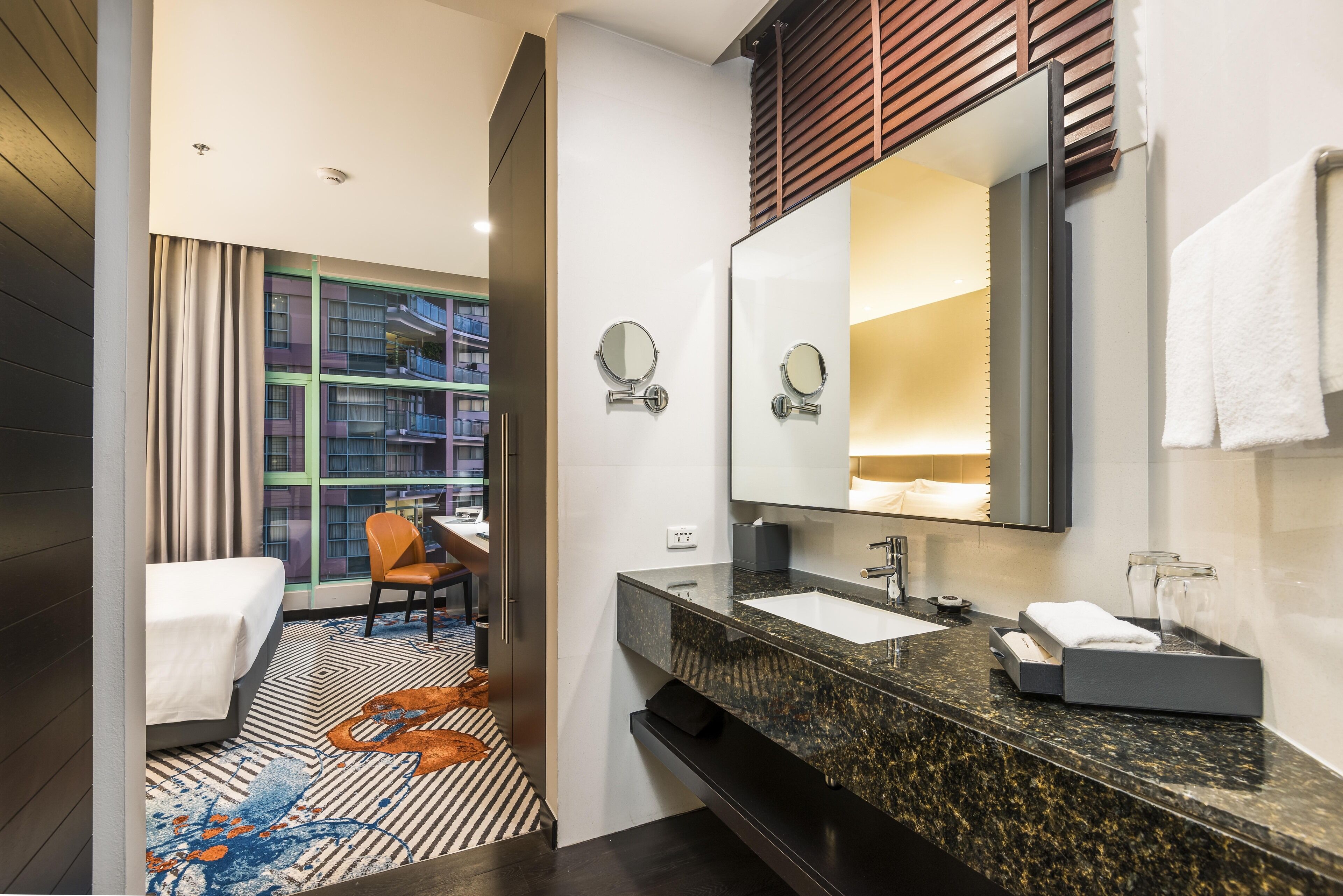 A modern hotel bathroom with a large mirror, a sink, and a shower.