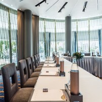 Un salón de conferencias con una larga mesa, sillas y un amplio ventanal con vistas al exterior.